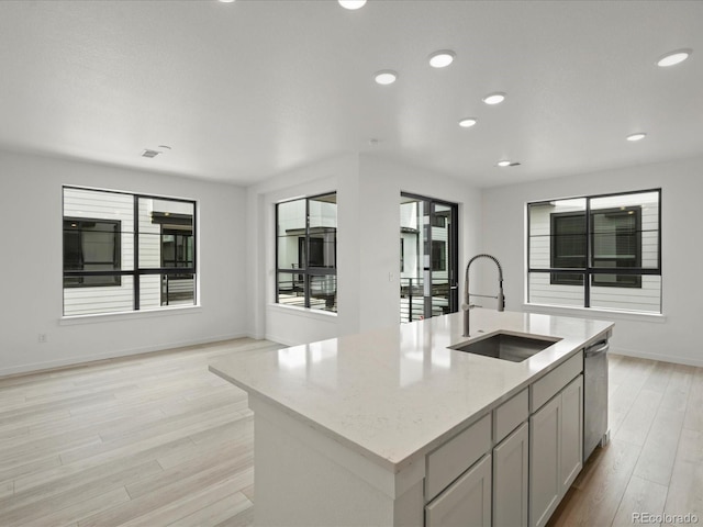 kitchen featuring a center island with sink, light wood-style flooring, open floor plan, light stone countertops, and a sink