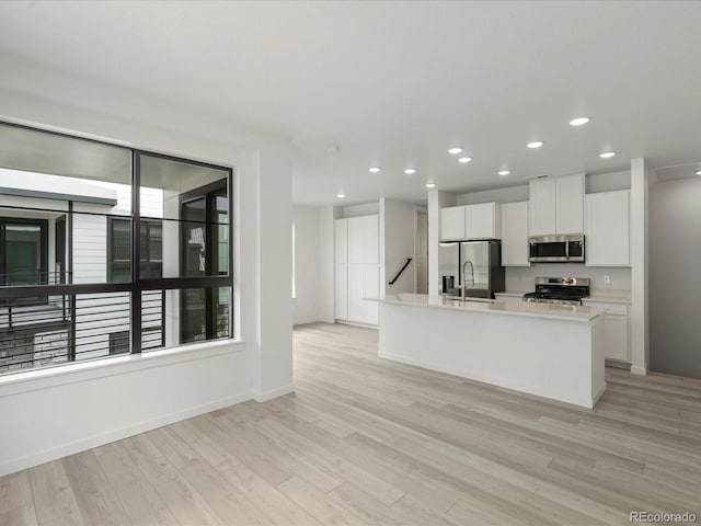 kitchen with a center island with sink, stainless steel appliances, light wood-style flooring, white cabinetry, and a sink