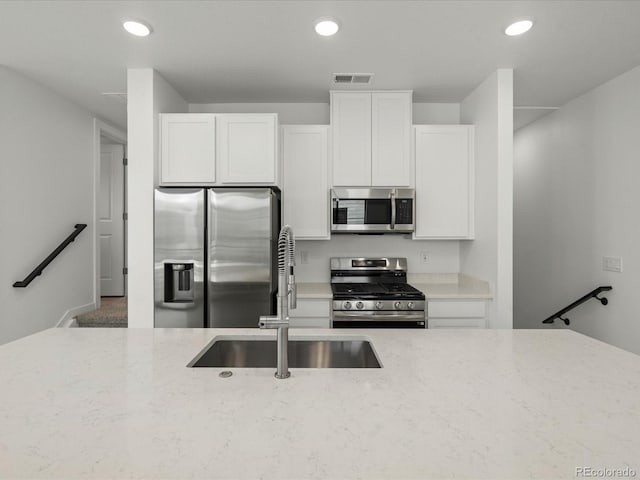 kitchen featuring stainless steel appliances, a sink, white cabinetry, and light stone countertops