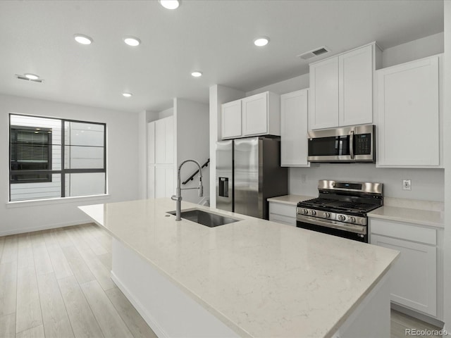 kitchen featuring appliances with stainless steel finishes, light stone counters, a kitchen island with sink, white cabinetry, and a sink