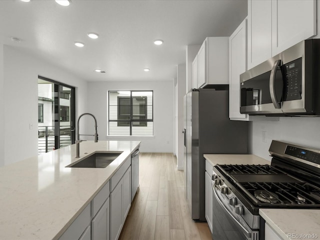 kitchen featuring stainless steel appliances, a sink, light wood-style flooring, and light stone countertops