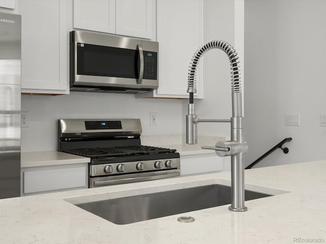 kitchen with stainless steel appliances, white cabinetry, and light stone counters