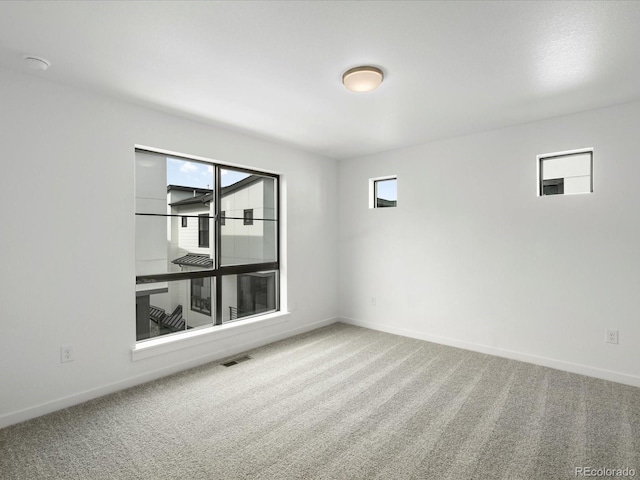 unfurnished room with carpet floors, visible vents, and baseboards