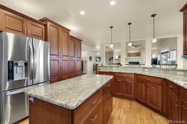 kitchen with stainless steel refrigerator with ice dispenser, light stone counters, ceiling fan, a kitchen island, and light wood-type flooring