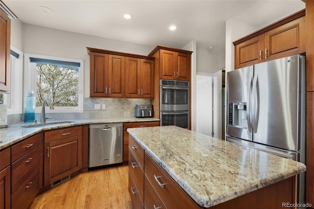 kitchen featuring appliances with stainless steel finishes, a sink, light stone countertops, light wood-type flooring, and recessed lighting
