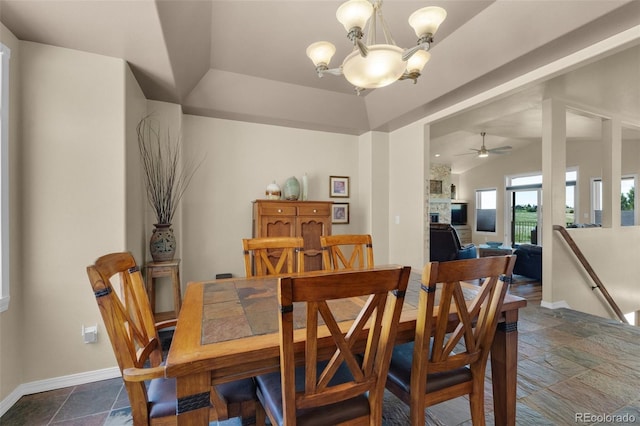 dining room with a chandelier, stone tile flooring, a ceiling fan, baseboards, and lofted ceiling