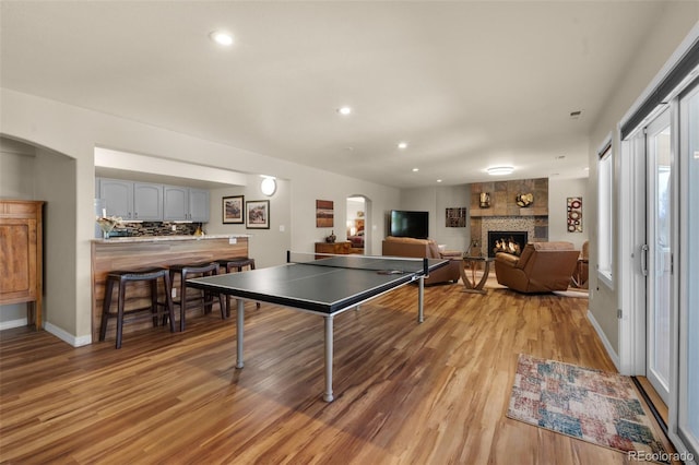 game room with arched walkways, a fireplace, light wood finished floors, recessed lighting, and baseboards