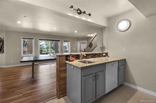 kitchen featuring white dishwasher, a sink, a peninsula, baseboards, and light stone counters