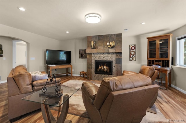living area with arched walkways, light wood-style flooring, a tiled fireplace, baseboards, and recessed lighting