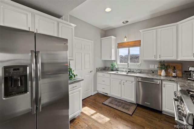 kitchen with dark wood finished floors, appliances with stainless steel finishes, white cabinetry, a sink, and light stone countertops