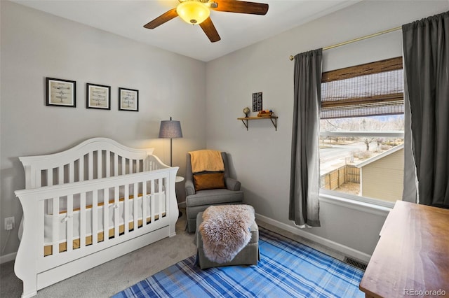 carpeted bedroom featuring a crib, visible vents, baseboards, and ceiling fan