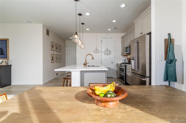 kitchen featuring sink, a breakfast bar area, a kitchen island with sink, high quality appliances, and pendant lighting