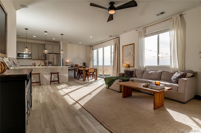 living room featuring light wood-type flooring, plenty of natural light, and ceiling fan