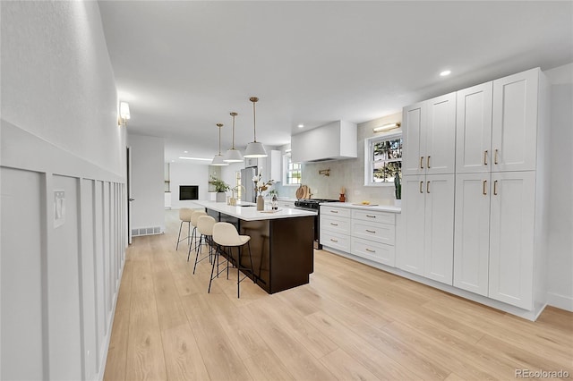 kitchen with light wood finished floors, a breakfast bar area, light countertops, white cabinetry, and stainless steel gas range