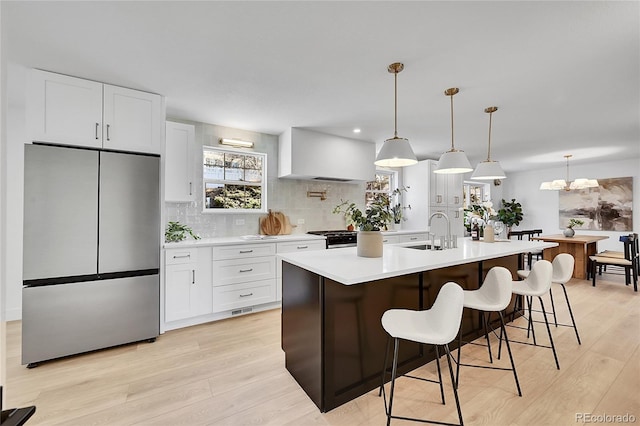 kitchen with a sink, light countertops, wall chimney range hood, freestanding refrigerator, and light wood finished floors