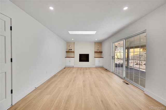 unfurnished living room featuring a skylight, baseboards, visible vents, light wood-style floors, and a fireplace