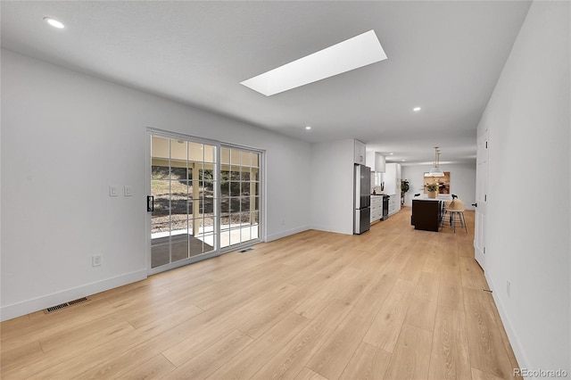 unfurnished living room featuring light wood-style floors, a skylight, visible vents, and baseboards