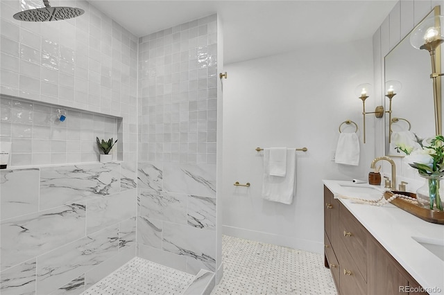 bathroom featuring a tile shower, double vanity, a sink, and baseboards