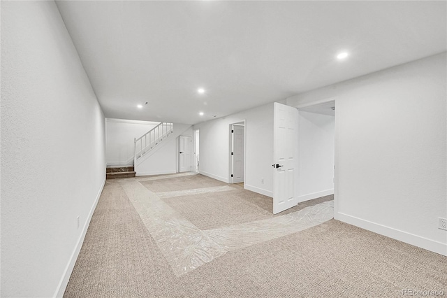 below grade area featuring light carpet, baseboards, stairway, and recessed lighting