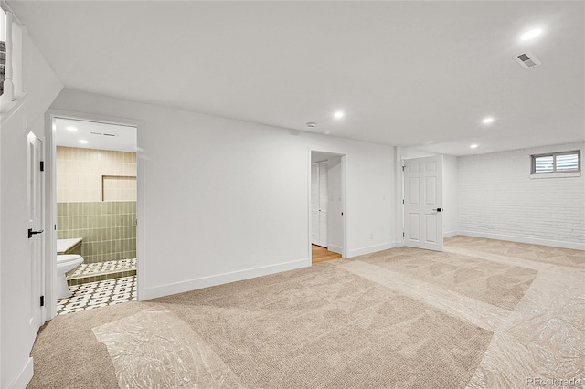 finished basement with light carpet, brick wall, visible vents, and recessed lighting