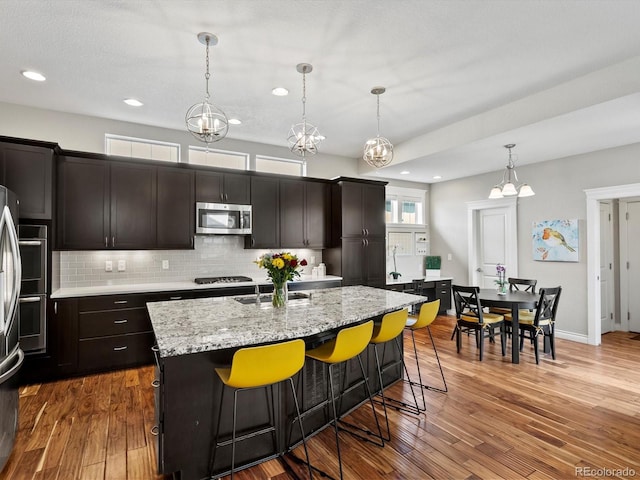 8012 E 50th Dr, Denver, CO 80238 - kitchen with stainless steel appliances, decorative backsplash, a kitchen breakfast bar, a kitchen island with sink, and hanging light fixtures