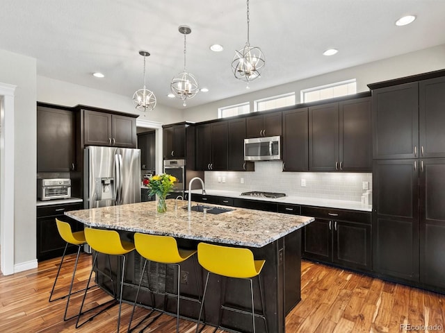 8012 E 50th Dr, Denver, CO 80238 - kitchen featuring stainless steel appliances, a kitchen bar, tasteful backsplash, a center island with sink, and light stone counters