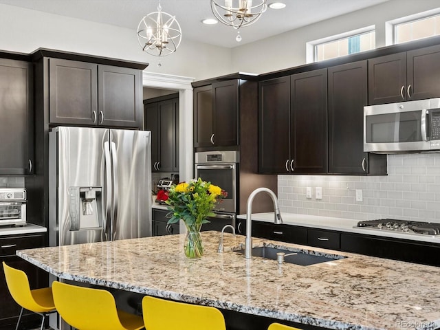 8012 E 50th Dr, Denver, CO 80238 - kitchen with stainless steel appliances, a chandelier, a kitchen bar, decorative backsplash, and light stone counters