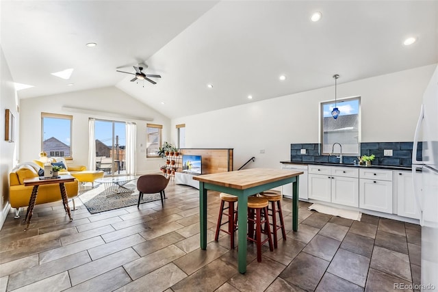 kitchen with lofted ceiling, white appliances, hanging light fixtures, ceiling fan, and white cabinetry