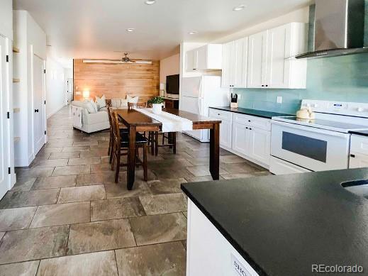 kitchen with wall chimney exhaust hood, white cabinetry, white appliances, and ceiling fan