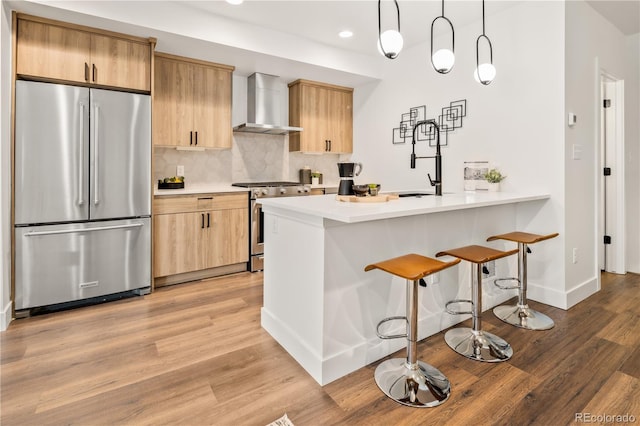 1344 N Knox Ct, Denver, CO 80204 - kitchen featuring stainless steel appliances, wall chimney exhaust hood, a kitchen bar, light countertops, and decorative backsplash