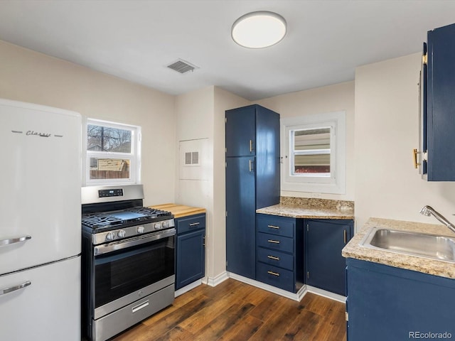 kitchen featuring white refrigerator, sink, blue cabinetry, and stainless steel gas stove