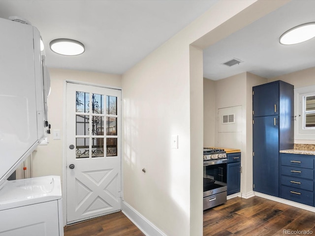 kitchen featuring blue cabinetry, stacked washer and dryer, stainless steel range with gas stovetop, dark hardwood / wood-style flooring, and light stone countertops