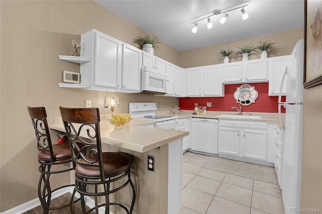 kitchen featuring a kitchen breakfast bar, white cabinetry, white appliances, light tile patterned floors, and sink