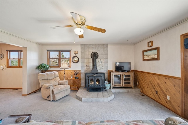 5245 Sapphire Dr, Colorado Springs, CO 80918 - carpeted living area featuring healthy amount of natural light, wood walls, a wood stove, ceiling fan, and a wainscoted wall