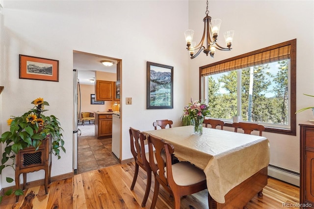 dining space with a notable chandelier, a high ceiling, baseboards, baseboard heating, and light wood finished floors