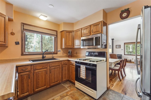 kitchen with appliances with stainless steel finishes, brown cabinetry, light countertops, and a sink