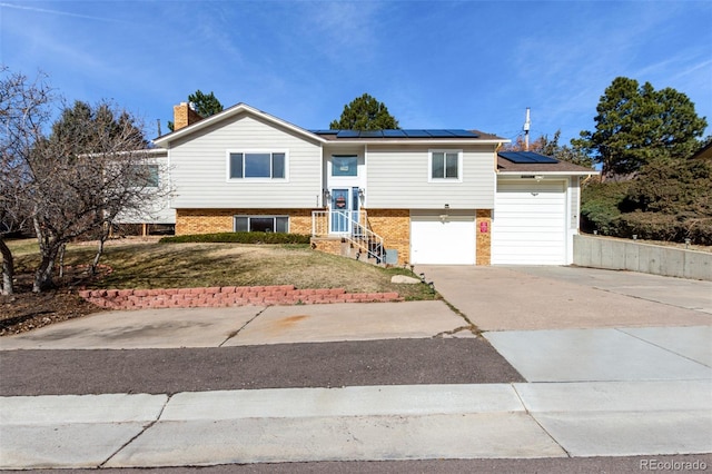 raised ranch featuring brick siding, roof mounted solar panels, driveway, and a garage