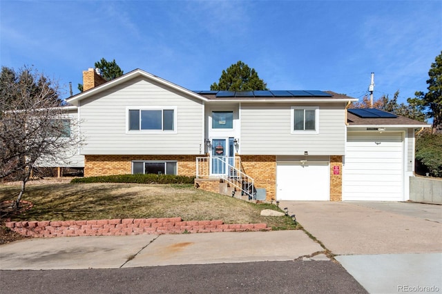 bi-level home featuring brick siding, solar panels, and driveway