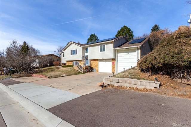 split foyer home with a garage, brick siding, solar panels, and concrete driveway