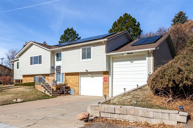 view of front facade featuring a garage, roof mounted solar panels, brick siding, and driveway