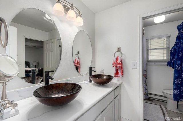 full bathroom featuring double vanity, toilet, baseboard heating, and a sink