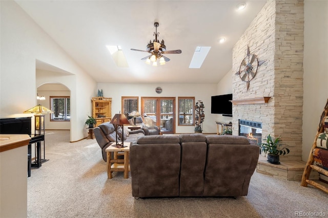 living room featuring a stone fireplace, vaulted ceiling with skylight, light carpet, and ceiling fan