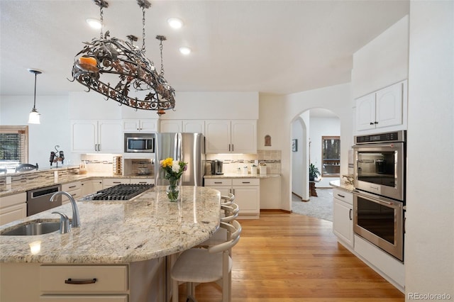 kitchen with sink, tasteful backsplash, decorative light fixtures, appliances with stainless steel finishes, and light stone countertops