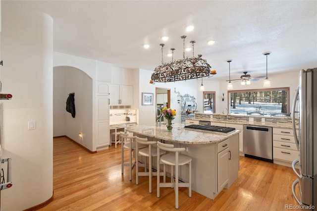 kitchen featuring a breakfast bar area, white cabinets, hanging light fixtures, a center island, and stainless steel appliances