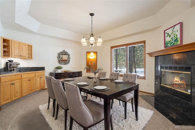 dining area featuring a tiled fireplace, a raised ceiling, and a chandelier