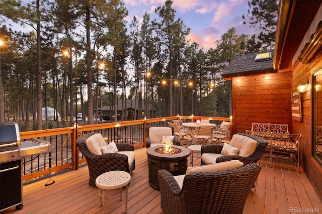 deck at dusk featuring area for grilling and an outdoor living space with a fire pit