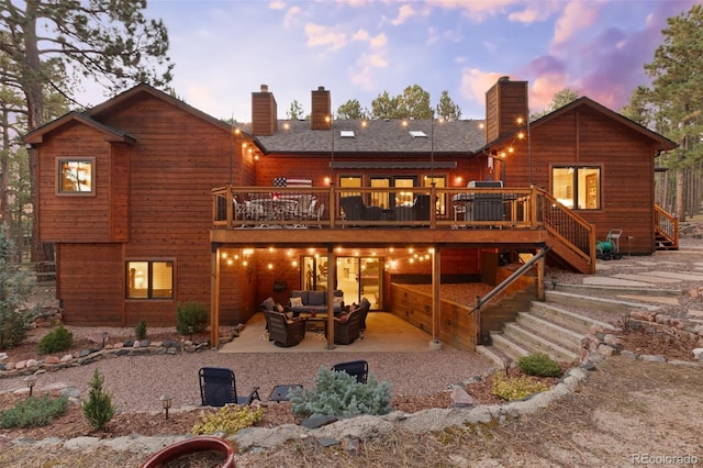 back house at dusk with outdoor lounge area, a deck, and a patio area