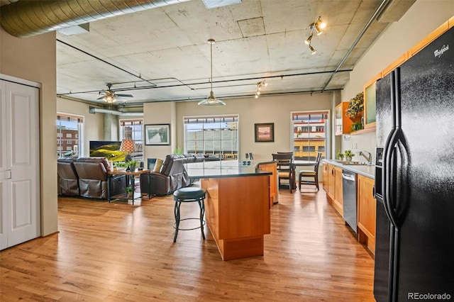 kitchen featuring black refrigerator with ice dispenser, light wood-type flooring, dishwasher, a kitchen island, and pendant lighting