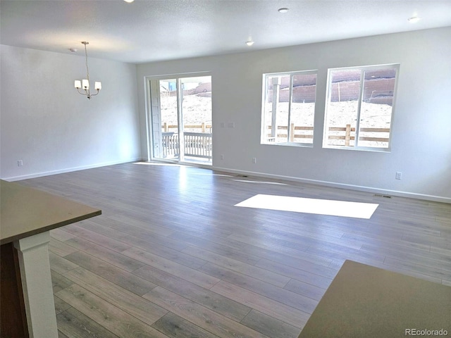 unfurnished living room with a chandelier, wood finished floors, and baseboards