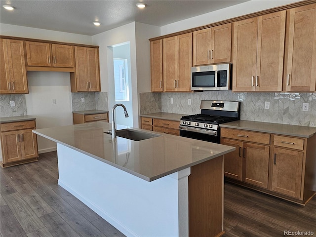 kitchen with appliances with stainless steel finishes, a sink, a center island with sink, dark wood-type flooring, and recessed lighting